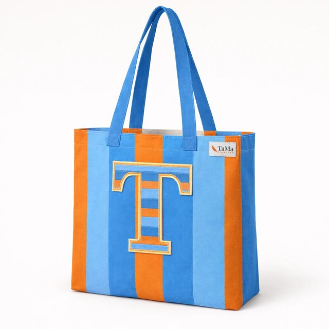Bolsa com listras laranja e azuis, letra T aplicada na frente, alças azuis e etiqueta com a marca TaMa.