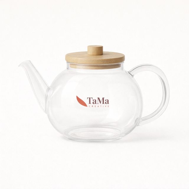 Bule bojudo transparente vazio, com bico longo, alça lateral e tampa em tom natural, com a marca TaMa nas cores oficiais no corpo.