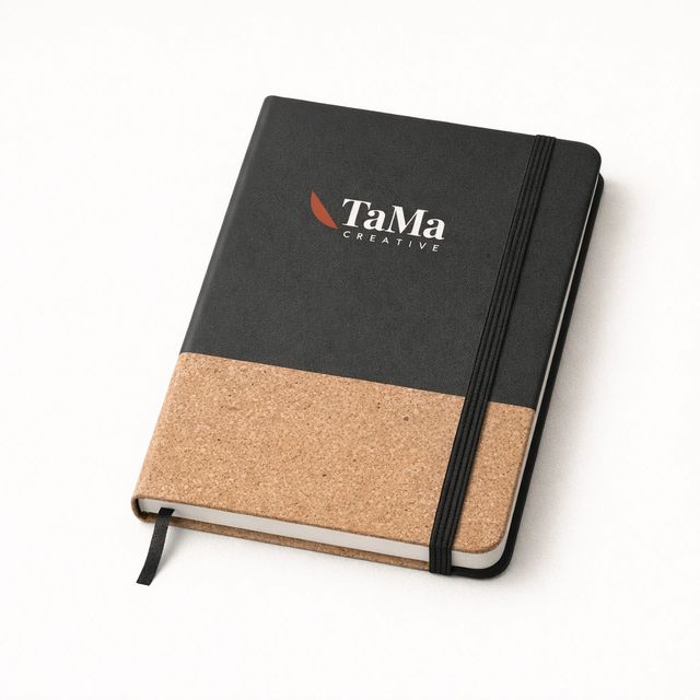 Caderno com capa bicolor, parte de cima preta e faixa inferior texturizada em tom natural, elástico preto, com a marca TaMa em branco, folha em vermelho, na capa.