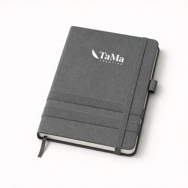 Caderno cinza com capa mesclada, faixas elásticas porta-celular e alça para caneta, com a marca TaMa em branco na capa.