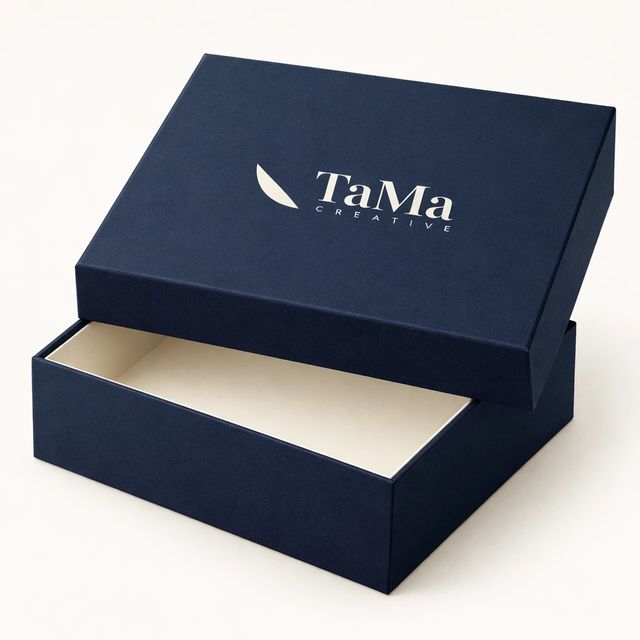 Caixa rígida com tampa e interior creme, na cor azul-marinho, com a marca TaMa na tampa.