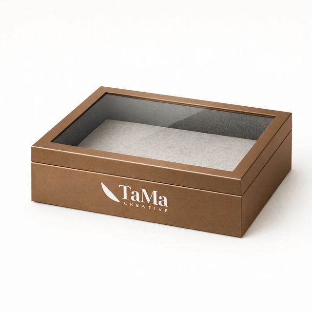Caixa para presente bronze com tampa transparente, vazia, com a marca TaMa em branco na lateral frontal.