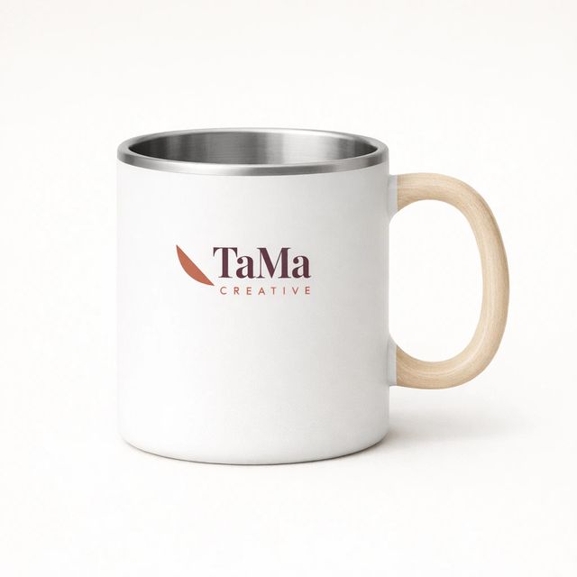 Caneca branca com alça em tom natural e interior prateado, com a marca TaMa nas cores oficiais no corpo.