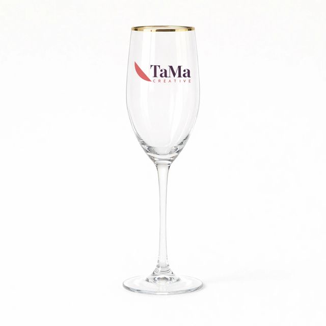 Taça flute transparente com borda dourada e a marca TaMa no bojo.