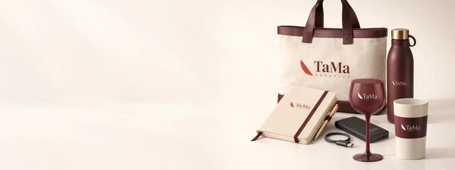 Ecobag de algodão cru com alças de couro bordô, squeeze bordô, caderno com caneta dourada, power bank, taça de gin bordô e copo personalizado, todos com a marca TaMa.