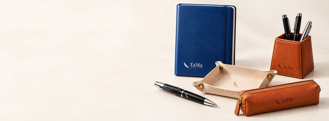 Caderno azul, canetas, porta-lápis, bandeja e estojo em couro com a marca TaMa.