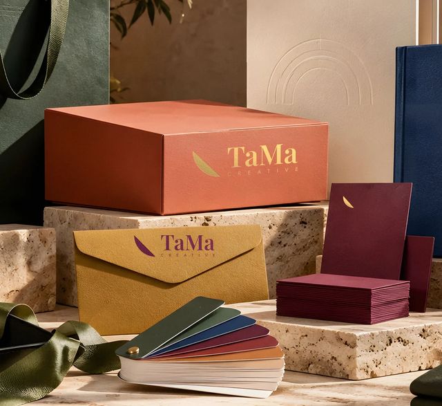 Kit de papelaria TaMa com caixa terracota com logo em hot stamping dourado, envelope mostarda com assinatura TaMa Creative em ameixa e cartão bordô com pétala dourada. Mockup ilustrativo.