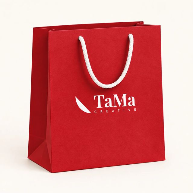 Sacola de presente com alças de cordão, na cor vermelha, com a marca TaMa na frente.