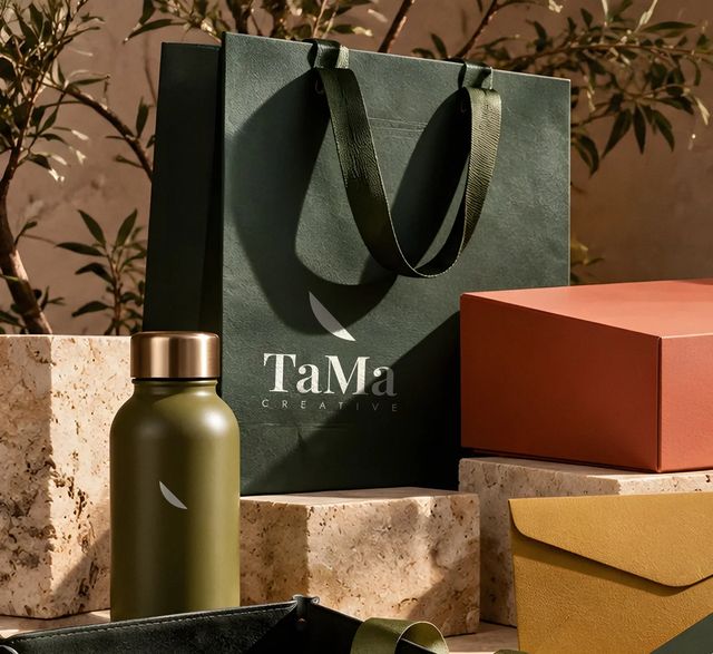 Sacola de papel verde com logo TaMa Creative impresso em creme e garrafa com pétala gravada a laser. Mockup ilustrativo.