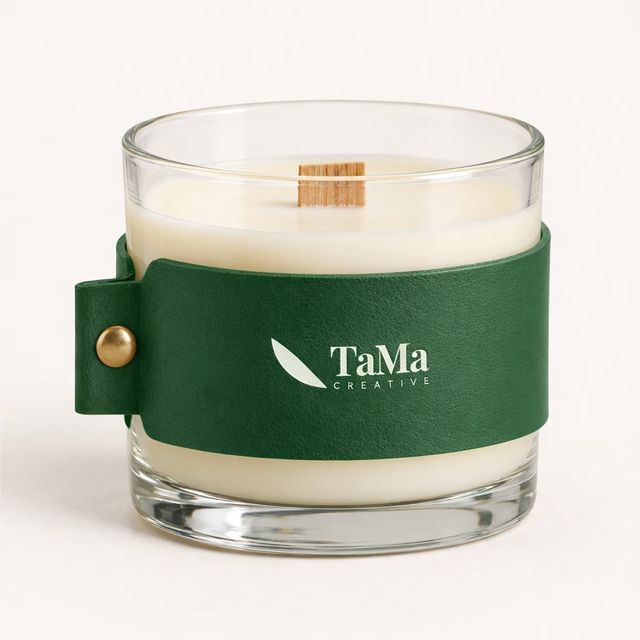 Vela aromática em copo, com cinta verde e pavio, com a marca TaMa na cinta.
